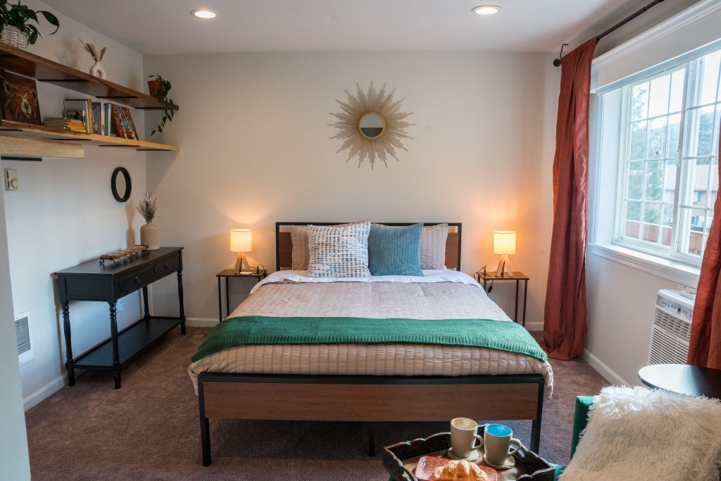 Une chambre à coucher comprenant un lit, des tables de chevet, une commode, une fenêtre avec des rideaux et un miroir fixé au mur.