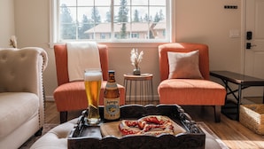 A cozy living room with two armchairs, a coffee table with a pretzel, a beer bottle, and a glass of beer.