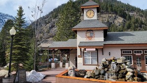 A lodge with a clock tower, a stone bench, and a waterfall feature.