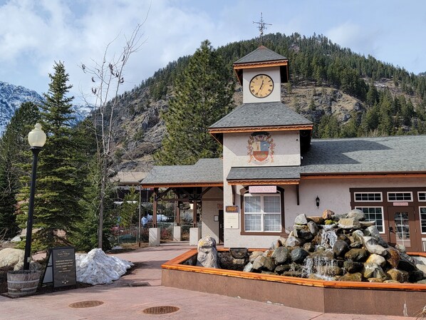 Una cabaña con una torre de reloj, un banco de piedra y una cascada.