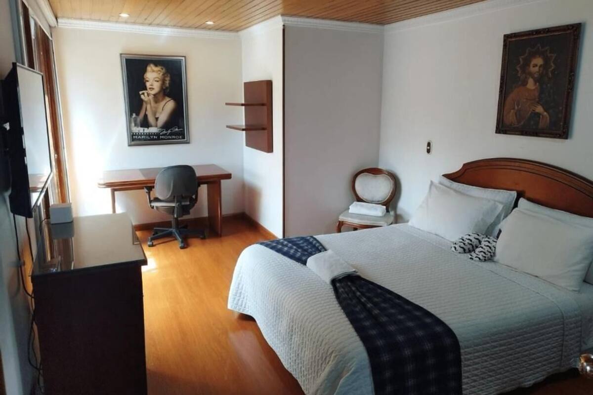 A bedroom with a bed, a desk, a chair, and a wooden ceiling.