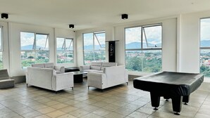 Una habitación amplia con ventanas grandes, mesa de billar y un conjunto de sofás.