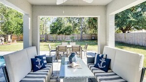 Une terrasse extérieure avec une table à plateau en verre, des coussins à rayures et une vue sur le jardin arrière.