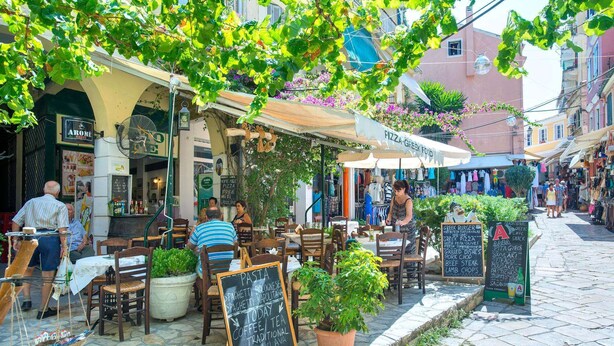 An outdoor café with tables and chairs, surrounded by potted plants and a street view. - Attractive Villa, A/C, Large Private Pool & Idyllic Setting in the Sought-After Area of Gastouri! (Kerkira)