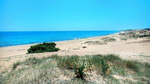 A beach with clear blue water, sandy dunes, and sparse vegetation. - Attractive Villa, A/C, Large Private Pool & Idyllic Setting in the Sought-After Area of Gastouri! (Kerkira)