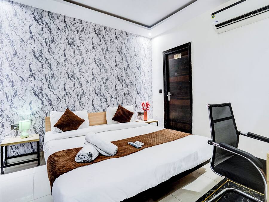 Une chambre d’hôtel avec un grand lit, un bureau avec une chaise, une table de chevet et un climatiseur fixé au mur.