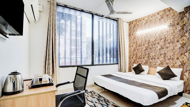 A hotel room with a bed, desk, chair, and a view of the city through large windows. - KINGS COURT HOTEL  (New Delhi)