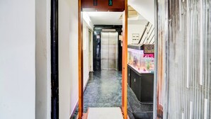 A hallway leading to an elevator with a sign indicating the direction of the exit. - KINGS COURT HOTEL  (New Delhi)