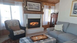 A cozy living room with a fireplace, a sofa, a chair, and a coffee table. - Tradewinds Cabin on Big Cormorant (Audubon)