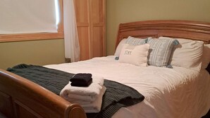 A bedroom with a wooden bed, a window with curtains, and a wooden wardrobe. - Tradewinds Cabin on Big Cormorant (Audubon)