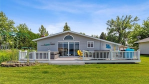 A single-story house with a deck, a fenced yard, and a clear sky. - Tradewinds Cabin on Big Cormorant (Audubon)