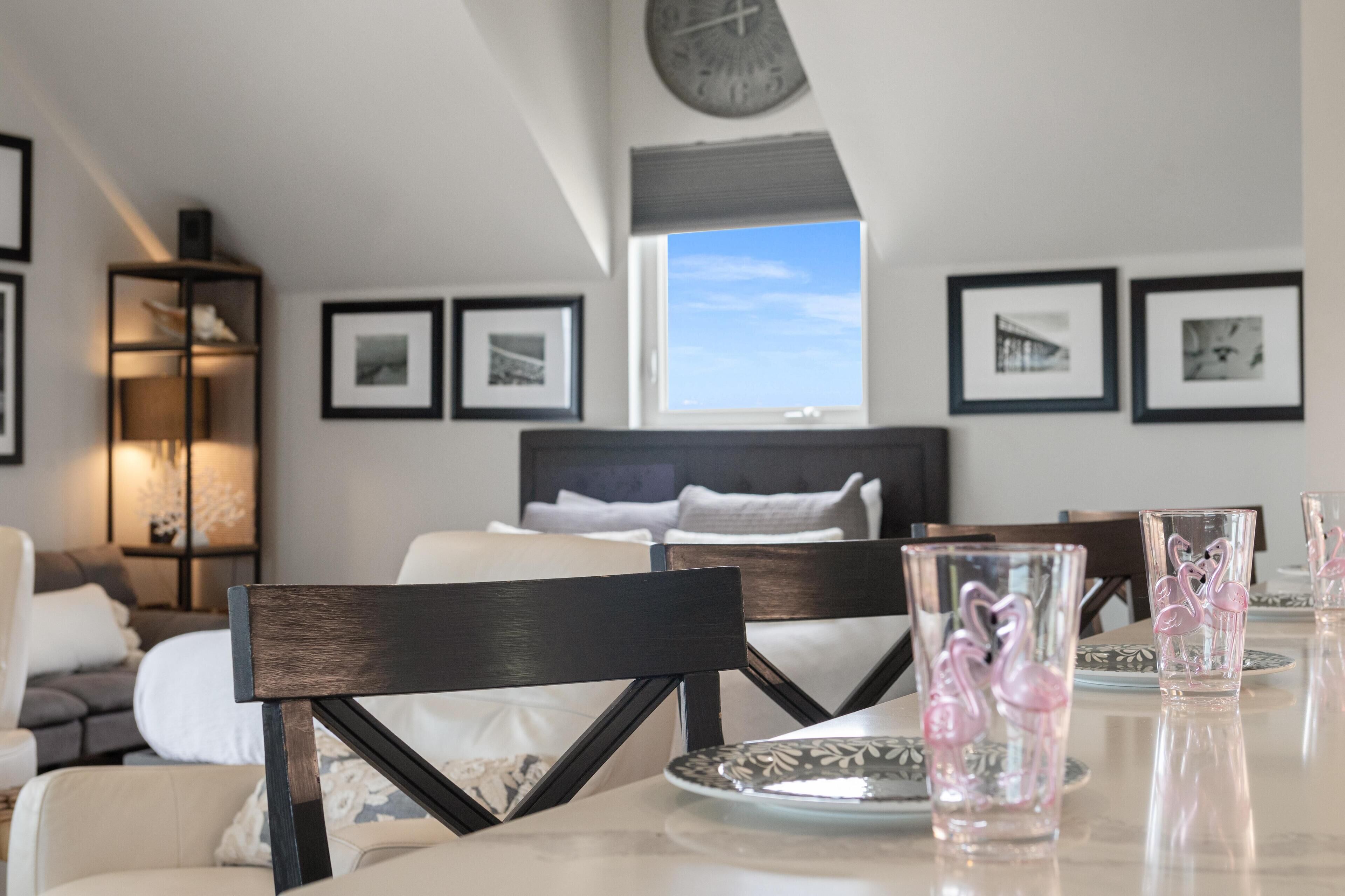 Ein modernes Hotelzimmer mit einem großen Bett, einem Esstisch mit Stühlen und gerahmten Bildern an den Wänden.