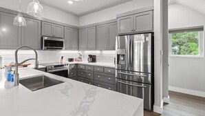 A modern kitchen with grey cabinets, stainless steel appliances, a marble island, and pendant lighting.