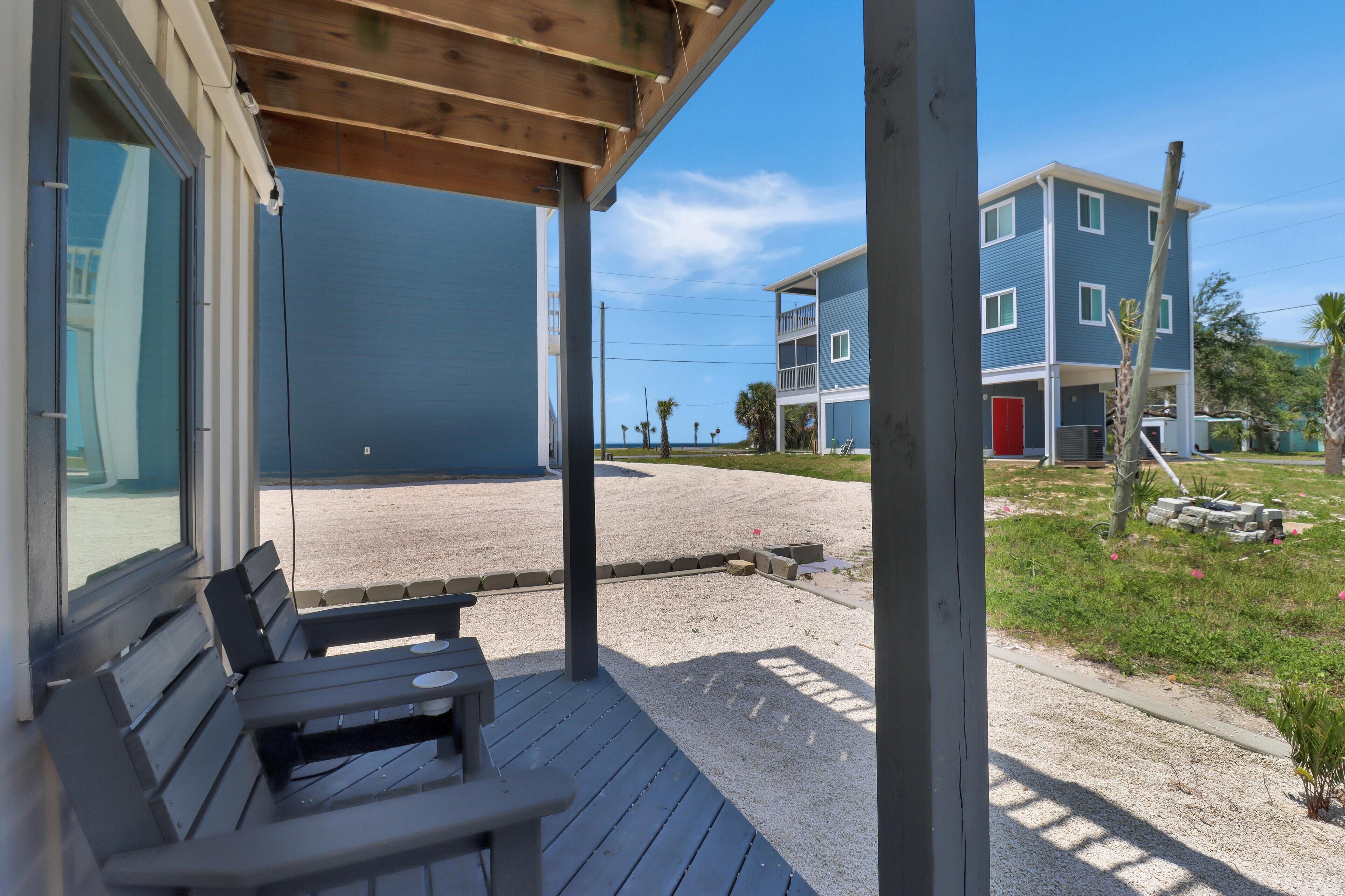 A covered outdoor seating area with benches, a view of a building with a red door, and a clear sky.