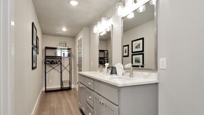 A modern bathroom with a large mirror, vanity, and a walk-in closet with a metal rack. - Sugar Sand Cottage B (Port St. Joe)