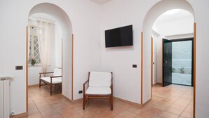A room with a TV mounted on the wall, a chair, and an open door leading to a balcony. - Donna Anna's House by Rentbeat (Civitavecchia)