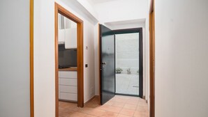 A narrow hallway with a kitchen area, a sliding glass door leading to an outdoor space, and a tiled floor. - Donna Anna's House by Rentbeat (Civitavecchia)