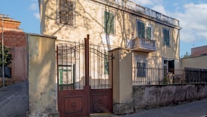 A two-story building with a gated entrance, a balcony, and a paved street. - Donna Anna's House by Rentbeat (Civitavecchia)