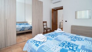 A bedroom with a bed, a chair, a wardrobe, and a mirror on the wall. - Donna Anna's House by Rentbeat (Civitavecchia)
