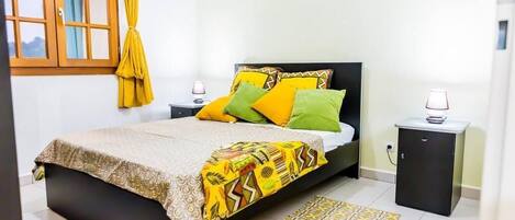 A bedroom with a bed, nightstands, a small cabinet, and a window with curtains.