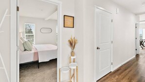 A hallway with a bed in a room, a door, and a small table with a vase. - Top floor corner condo with UNREAL views of Commencement Bay + DT Tacoma skyline (Tacoma)