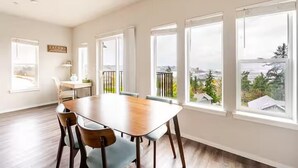 A dining area with a wooden table and chairs, large windows with curtains, and a view of a cityscape. - Top floor corner condo with UNREAL views of Commencement Bay + DT Tacoma skyline (Tacoma)