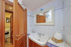 Une salle de bain avec une porte en bois, un lavabo blanc, un miroir et un porte-serviettes.
