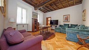 Un salon avec un parquet en chevrons, des poutres apparentes en bois au plafond, un canapé, une causeuse, un téléviseur et un canapé vert.