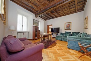 Un salon avec un parquet en chevrons, des poutres apparentes en bois au plafond, un canapé, une causeuse, un téléviseur et un canapé vert.