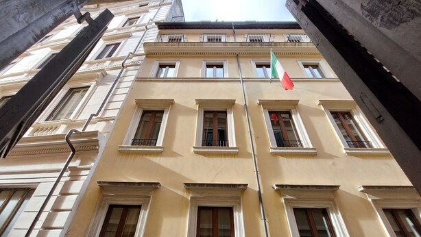 Un immeuble à étages doté d’une façade symétrique, de grandes fenêtres et d’un mât sur lequel flottent des drapeaux.