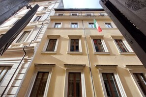 A multi-story building with a symmetrical facade, large windows, and a flagpole with flags.