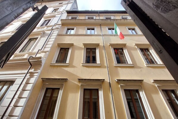 A multi-story building with a symmetrical facade, large windows, and a flagpole with flags.