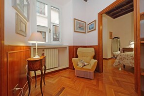 Une pièce avec un plancher en bois, une lampe, une chaise avec un livre, un lit et une fenêtre donnant sur un beau paysage.