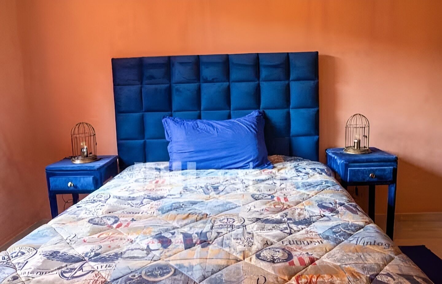 A bed with a blue headboard and a patterned bedspread, flanked by two nightstands with birdcages.