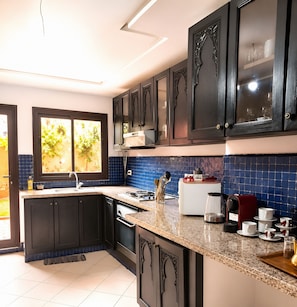 Cozinha moderna com armários escuros, bancada de granito e vista para o exterior.
