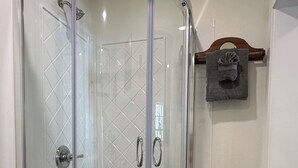 Una cabina doccia in vetro con parete rivestita di piastrelle a motivo a diamante, soffione e mancorrente.