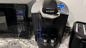 Una macchina da caffè Keurig su un piano di lavoro in granito, con un forno a microonde e un tostapane nelle vicinanze.