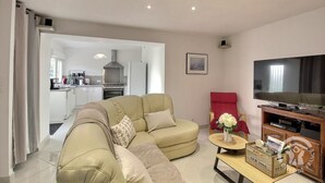 A modern living room with a beige sofa, a red armchair, a flat-screen TV, and a small table with a vase of flowers.