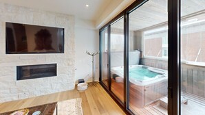 Ein modernes Interieur mit einer Steinwand, einem Flachbildfernseher, einem Kamin und einem gläsernen Whirlpoolbereich.