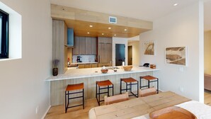 Eine moderne Küche mit Holzausstattung, einer zentralen Kochinsel mit Barhocker und einem Essbereich mit Holztisch und Bänken.