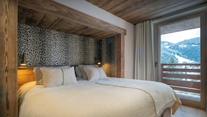 Un dormitorio con una cama grande, vigas de madera en el techo, cabecera de estampado de leopardo y vistas a montañas nevadas.