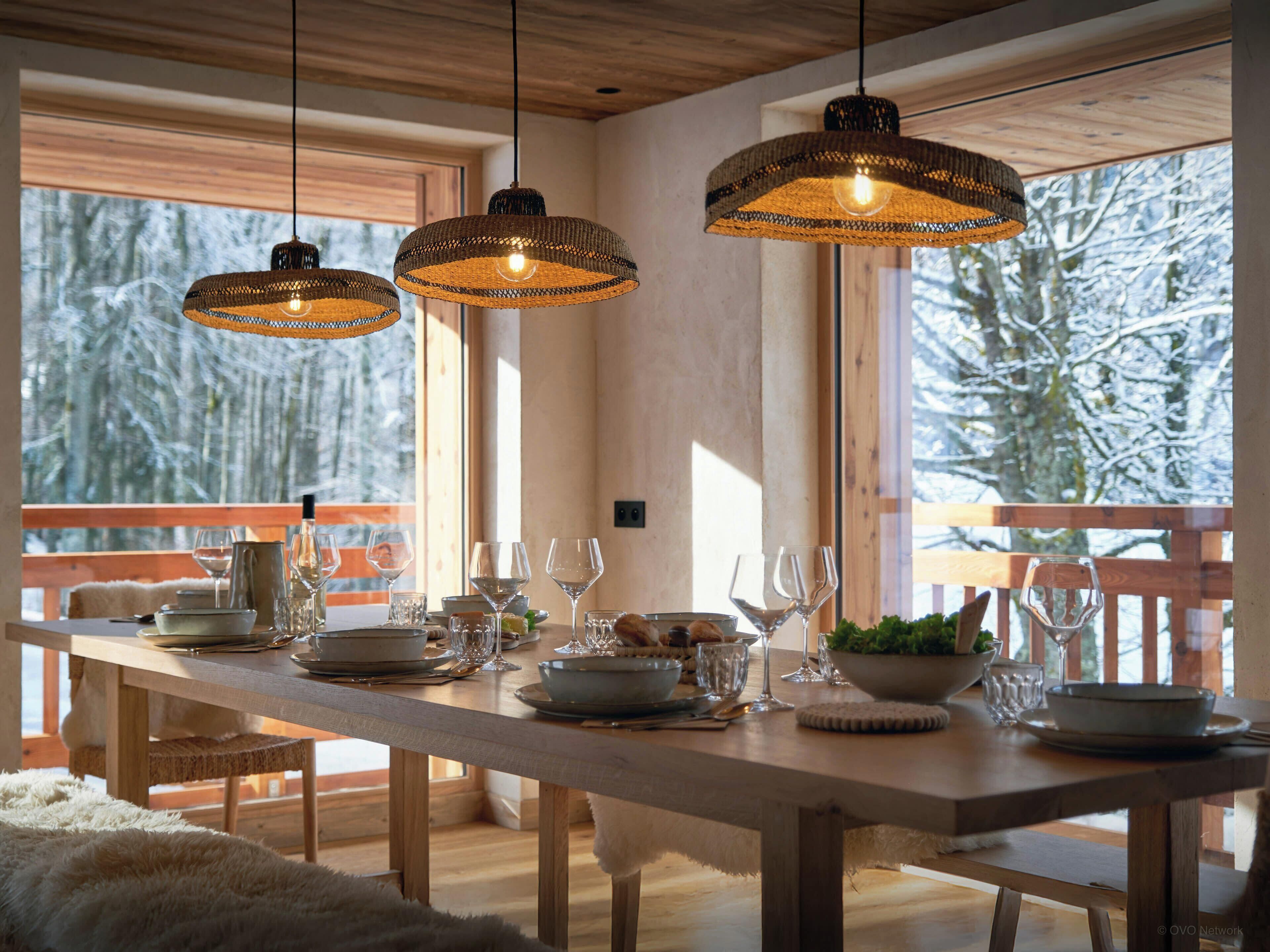 A dining area with a wooden table set for a meal, surrounded by large windows with a snowy landscape view.