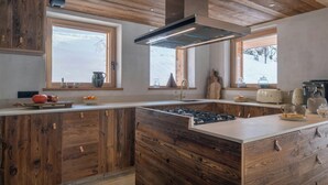 Una cocina moderna con armarios de madera, una isla central con estufa y grandes ventanales que aportan luz natural.