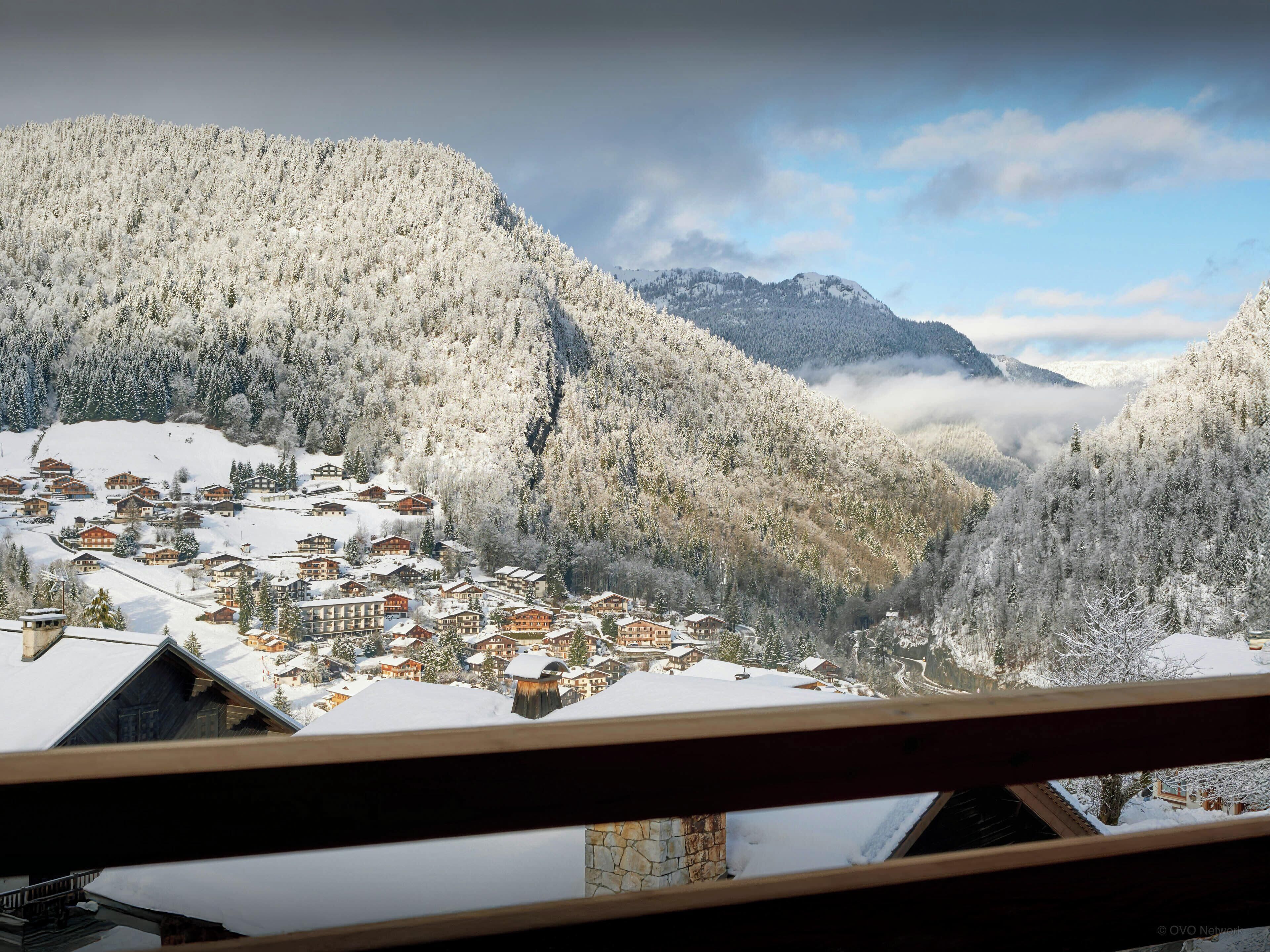 A snow-covered mountain village with traditional wooden houses and a view of the valley.