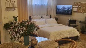 Une chambre moderne avec un grand lit, une télévision et un coin repas aménagé avec des meubles en osier.