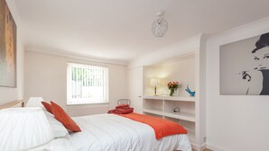 Ein Schlafzimmer mit Bett, Nachttisch, Lampe, Fenster, einer Regal mit Dekoration und einem Gemälde an der Wand.