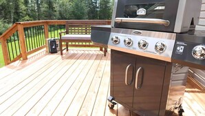 A Cuisinart grill on a wooden deck with a bench and a trash can. - Hare Hideaway with Fireplace (Prince Edward Island)