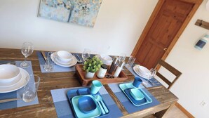 A dining table set with blue plates, glasses, and cutlery, a centerpiece with greenery, and a wooden tray with condiments. - Hare Hideaway with Fireplace (Prince Edward Island)