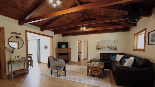 A spacious living room with a fireplace, a leather sofa, a television, and a wooden ceiling. - Hare Hideaway with Fireplace (Prince Edward Island)