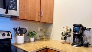 Une cuisine avec des meubles de rangement en bois, une cuisinière, une machine à café et une plante posée sur le plan de travail.